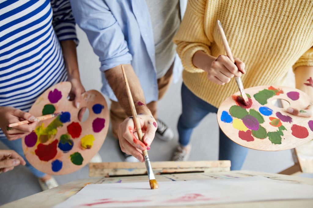 Overview of man with paintbrush teaching his students with color palette how to paint professionally