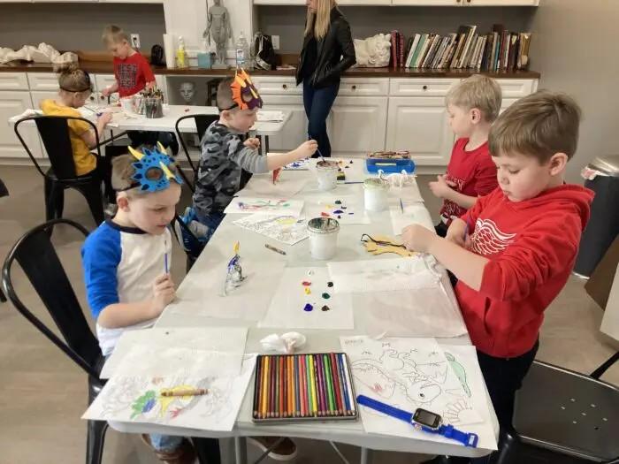 Children gathered around a table, creating art with paper and crayons during a summer activity.