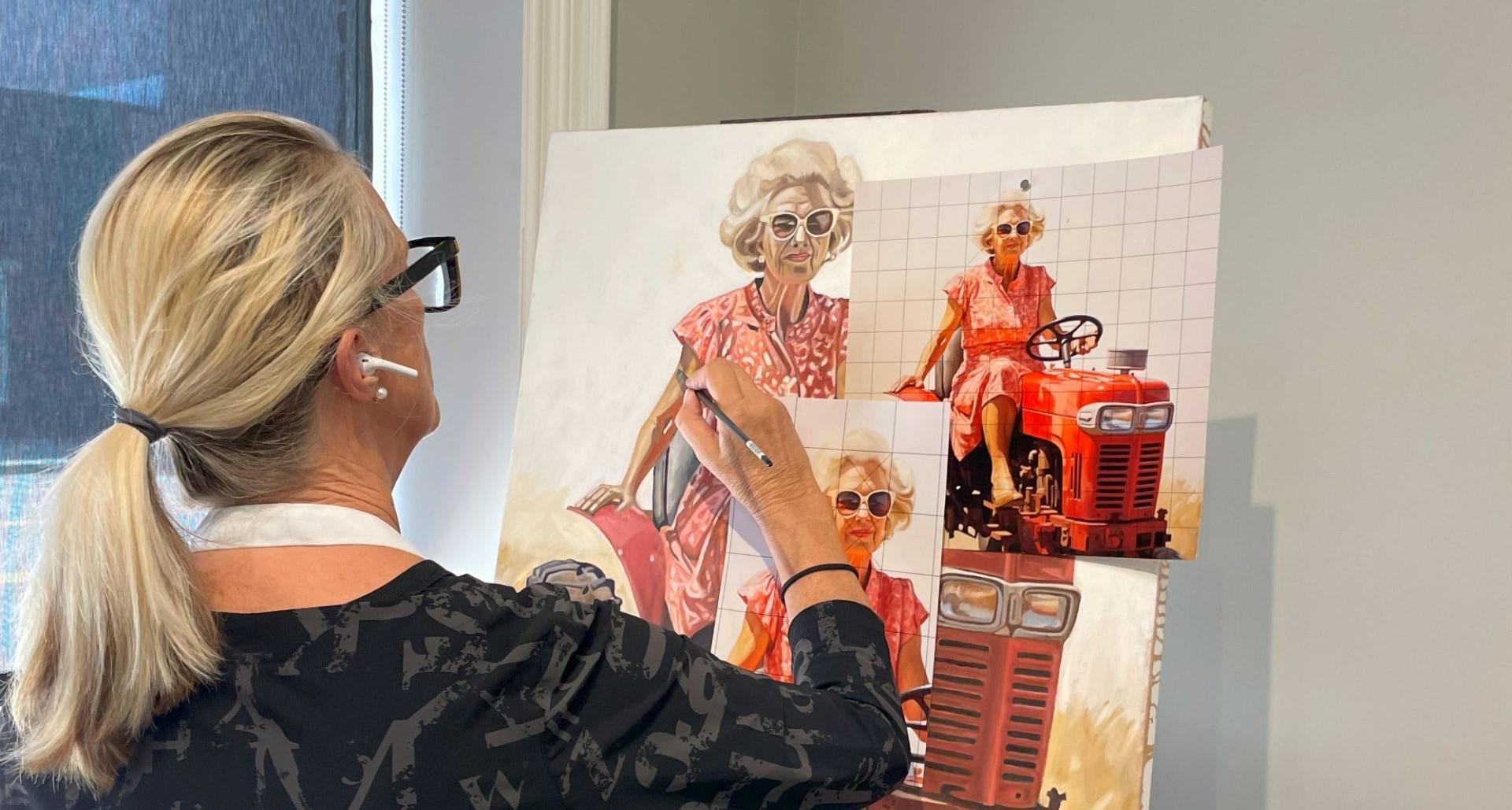 Person painting a portrait on a canvas with a grid overlay, using a reference photo pinned to guide the artwork—an example of how art classes in Royal Oak enhance thinking and perspective.