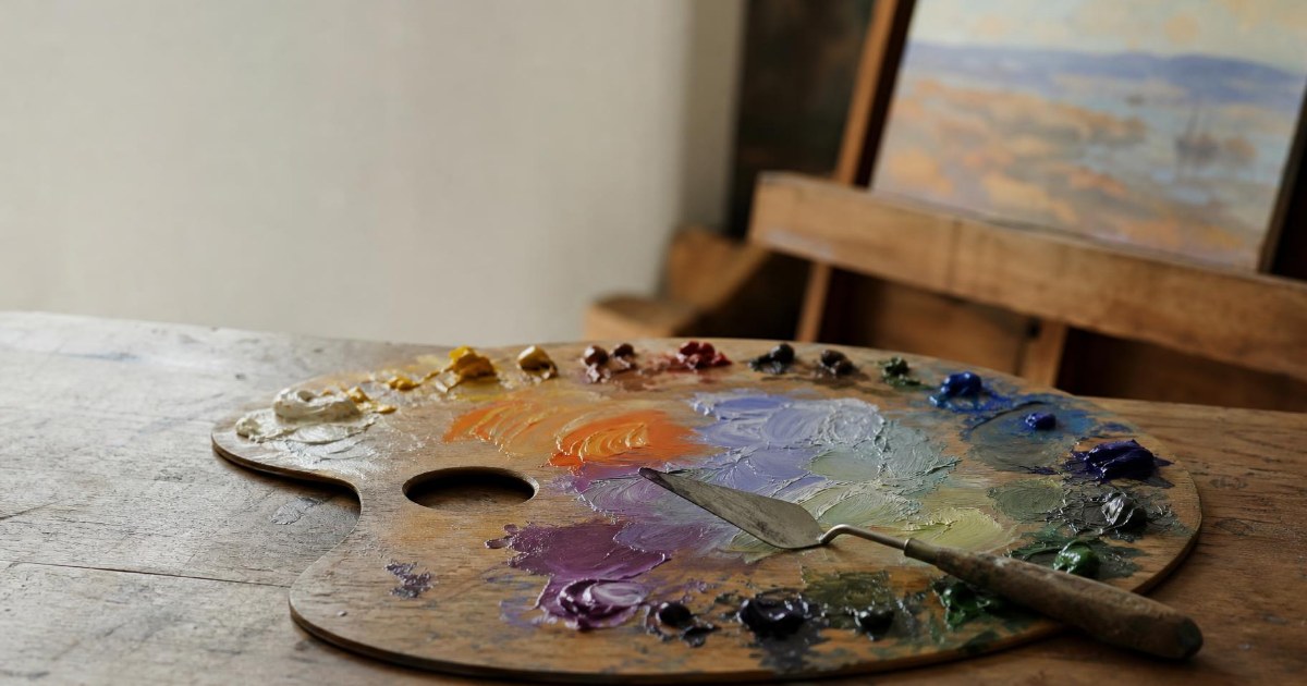 An oil painting palette with freshly mixed colors and a palette knife on a studio table in soft window light.