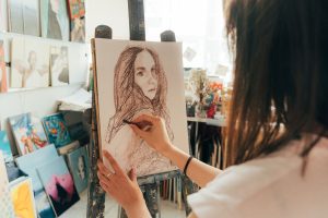 Artist drawing a charcoal portrait on an easel in a bright art studio